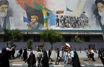 Iranian worshippers walk past a mural showing the Ayatollah Ali Khamenei, left, after Friday prayers in Tehran, 19 April, 2024