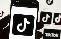 The TikTok logo is displayed on a mobile phone in front of a computer screen which displays a TikTok home page in Boston, 7 May, 2024