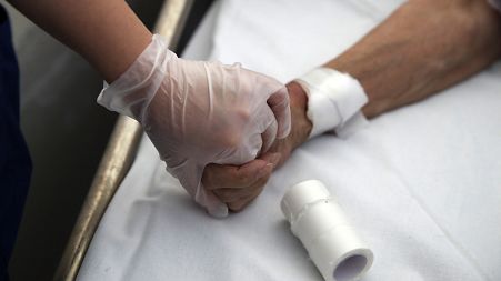 A medical worker holds the hand of a patient in Greece in 2020.